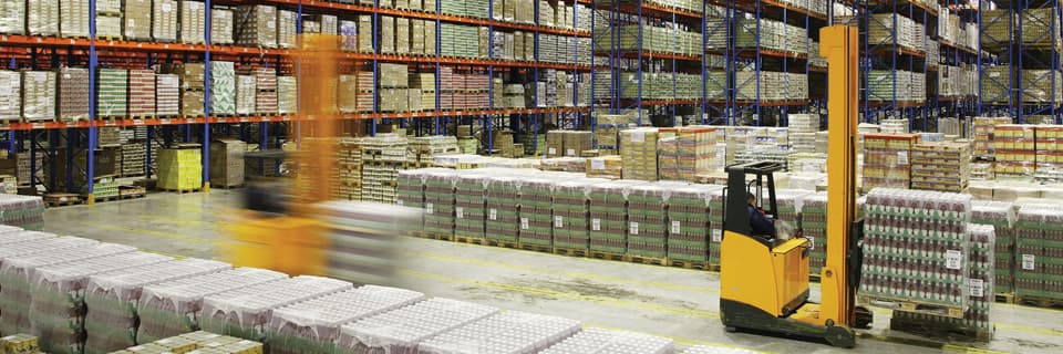 Forklifts moving palletized goods between high storage racks in a transload warehouse